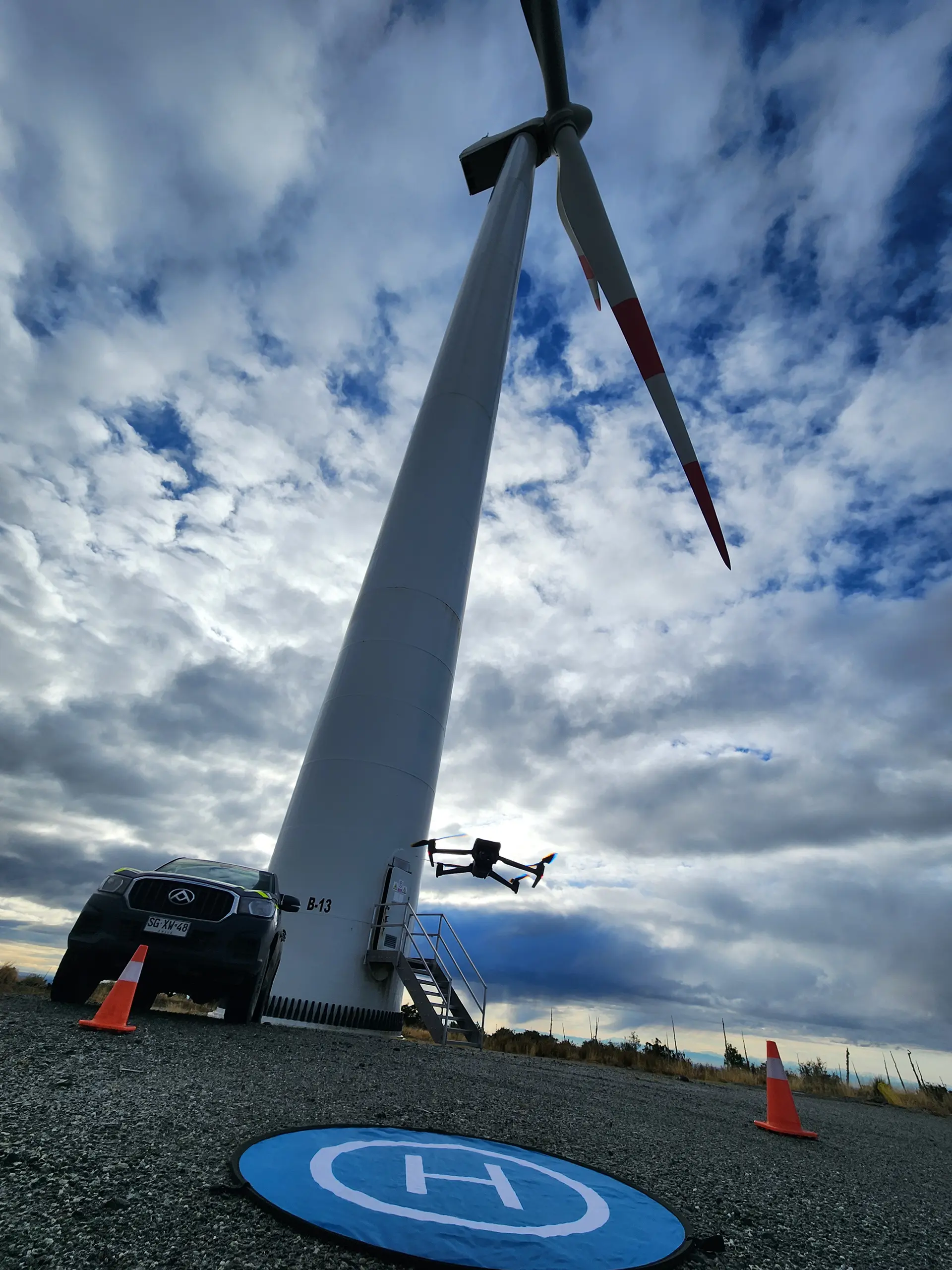 Dron elevándose para inspección con aerogenerador de fondo