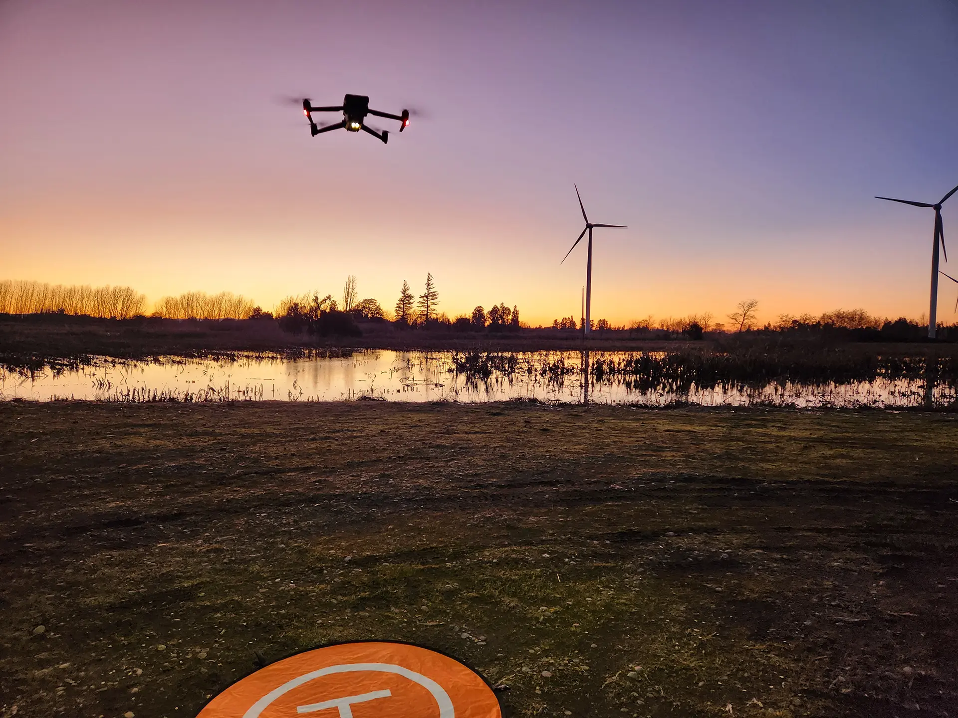 Dron realizando inspección al atardecer en parque eólico